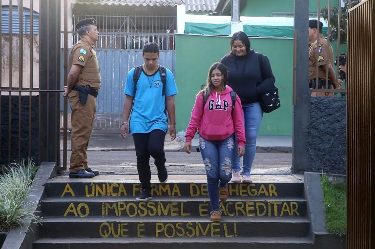 Policiais vigiam portão de escola por onde passam duas meninas e um menino